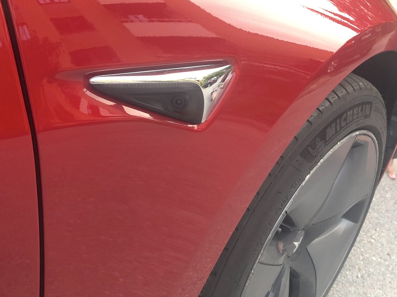 Close-up of the camera housing in the front wing of a red Tesla Model 3